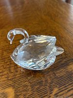 Clear faceted Swarovski crystal swan figurine displayed on wood surface, side angle showing detailed crystal facets and curved neck.