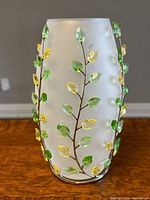 Full view of frosted vase mounted in metal vine with alternating green and yellow crystal leaves placed on wooden surface.