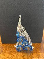 Front view of clear crystal peacock figurine with blue crystal flowers against black backdrop