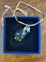 Green crystal Swarovski ornament with silver star and snowflake details inside a blue presentation box with black lining, attached to golden hanging ribbon.