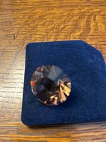 Close-up photo of a faceted round gold-tone Swarovski crystal chaton on a dark blue velvety surface, showing sparkle and reflective facets.