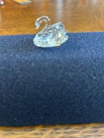 Small clear crystal swan figurine resting on dark fabric, showing side profile and sparkle.