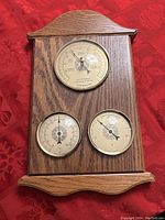 Full view of wooden weather plaque with three round dials: barometer on top, thermometer and hygrometer below.