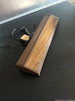 Closed view of 16-inch aquarium fluorescent strip light with brown frame and wood grain design on top, showing power cord and label attached.