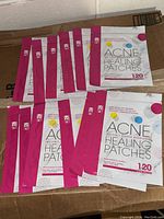 Ten resealable pouches of KG brand Acne Healing Patches with bright pink edges and white packaging, each containing 120 clear patches.