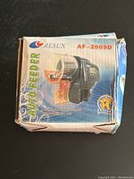 Photo of the front side of the box showing the 'Resun AF-2009D Auto Feeder' with an image of the feeder unit and text highlighting simple feeding adjustment and up to 4 times a day feeding.