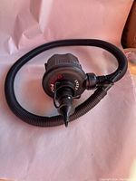 Photo of black Intex Quick-Fill battery air pump with attached flexible hose and nozzle lying on a surface.