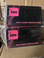 Two sealed black packages with pink labels, each marked 'pc 500' and '100% CLEAR ACRYLIC NAILS' indicating quantity and product type