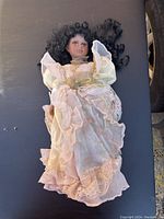Front view of collectible doll dressed in pink layered dress with lace and pearl necklace, lying down.