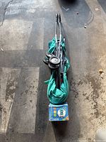 Folded green fabric Cosco umbrella stroller with visible wheels and handles taken from above.