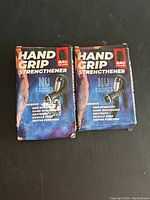 Two hand grip strengtheners in their original boxes showing front packaging with product details and brand logo.