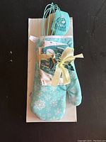 Photo of entire kitchen set wrapped with ribbon, showing oven mitt, potholder, spatula, and whisk on a white box