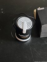 Top view of cylindrical black and white portable speaker with 'Fulfillment' label and attached lanyard.