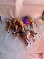 Three plastic toy horses spread out on a sheet, shows details of color and accessories like purple saddle and violin prop.