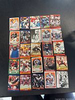 Layout of 25 football trading cards on black surface showing multiple players and teams.