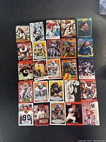 Top view of 25 football cards laid flat on black surface, showing colorful photos of players in action poses with team uniforms and logos of different brands like Fleer and Topps.