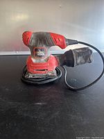 Front and side view of Black & Decker orbital sander including power cord and dust collection bag.