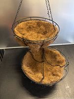Two stacked round metal hanging baskets shown upright with coconut fiber liners and suspension chains attached.