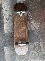 Top view of the wooden skateboard deck showing wood grain and wear marks, mounted with metal trucks and black wheels.