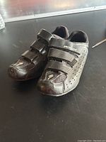 Pair of black men's cycling shoes with perforations and Velcro straps seen from side angle.