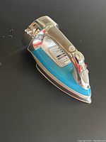 Side angle of the blue and chrome Hamilton Beach Steam Master iron resting on a black surface, showing the iron soleplate and handle.