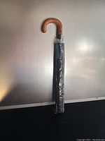 Full view of wrapped umbrella showing entire length with wooden curved handle and black wrapped canopy.