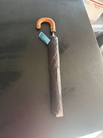 Photo of full folded black umbrella with curved wooden handle on a black surface.