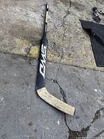 Full view of the vintage wooden hockey stick showing length and taped blade lying on concrete ground.