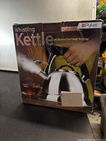 Box showing the front and side of the Pykal whistling kettle with a hand holding the handle and steam coming out of the spout, highlighting the cool-handle technology.