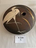 Front view of disc-shaped vase showing silver inlaid heron and gold reed accents around central opening