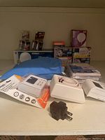 Image of assorted household electrical items including a small travel iron covered in blue cloth, electrical plugs, batteries, and lightbulbs stacked on a shelf.