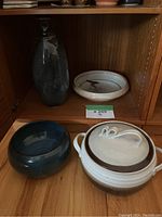 Photo of four vintage pottery pieces displayed in wooden shelving: tall vase, shallow bird plate, blue bowl, and covered pot