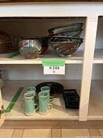 Shelf showing stacked bowls with brown designs, black and turquoise mugs, and black segmented trays.