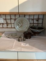 The lot of brown pottery and glass items arranged on a white surface against a tiled backsplash, showing all items and their details.