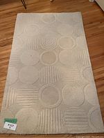 Photo showing cream throw rug fully unrolled on hardwood floor, highlighting circular and linear geometric patterns.