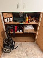 Wide view of laundry room cupboard with golf accessories and push cart inside.