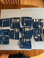 Overhead view of multiple blue cloth rolls containing assorted sterling silver flatware pieces including knives, forks, spoons and serving utensils