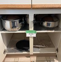 Open kitchen cupboard showing large and medium stainless steel pots on top shelf with lids.