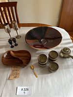 Overview of all serving items on white tablecloth including ceramic bowls and cups, teak serving tray, silver goblets, blue glasses, gold spoon and teapot.