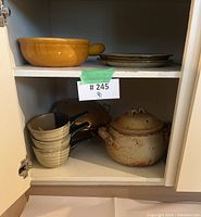 Kitchen cupboard interior shelves with vintage pottery and brass items grouped