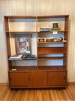 Front view of assembled two-piece mid-century modern teak entertainment unit showing upper open shelving and lower cabinet.