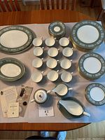 Top view of entire Wedgwood 'Asia' china set arranged on table showing plates, cups, saucers, creamer, and covered sugar bowl with informational pamphlets.