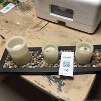 Front view of flameless candle set showing candles aligned on pebble-filled black tray.