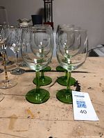 Front view of six clear wine glasses with green stems and bases arranged in two rows.