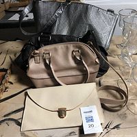 Four purses on wooden table showing cream clutch with gold clasp, beige handbag, black handbag, and metallic silver shoulder bag.