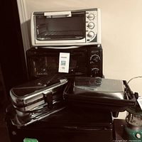 Two stacked toaster ovens (one white Black & Decker on top and one black Bravetti below) with panini sandwich maker and waffle iron at front.