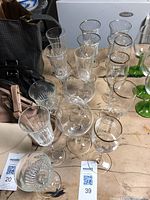 Miscellaneous assortment of clear and green stemmed wine glasses on a wooden surface alongside handbags.