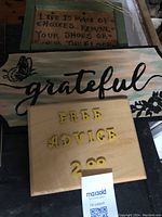 Photo showing three handmade wooden signs including one with 'grateful' in cursive, one with a life choices quote, and a wooden board with yellow letters for free advice.