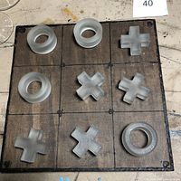 Wooden tic tac toe board with frosted glass X and O pieces arranged in playing patterns on the grid, photo taken to show the board and pieces setup.
