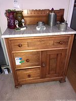 Front view of Victorian Eastlake washstand showing marble top and wooden base with three drawers and one cabinet door, with items on top.
